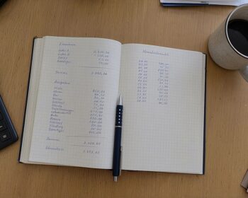Aufgeschlagenes Notizbuch mit handschriftlichen Zahlenspalten auf einem Schreibtisch