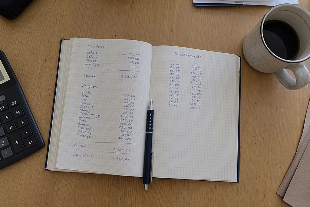 Aufgeschlagenes Notizbuch mit handschriftlichen Zahlenspalten auf einem Schreibtisch